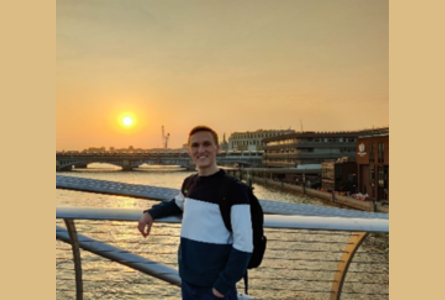 Image of a person standing on a bridge at sunset, smiling at the camera